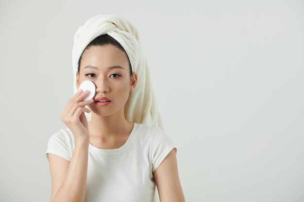 Portrait de jeune femme essuyant le toner sur le visage avec un coton pour restaurer le niveau de ph de la peau