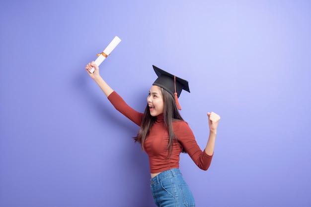 Portrait de jeune femme étudiante à l'Université avec chapeau de graduation sur fond violet