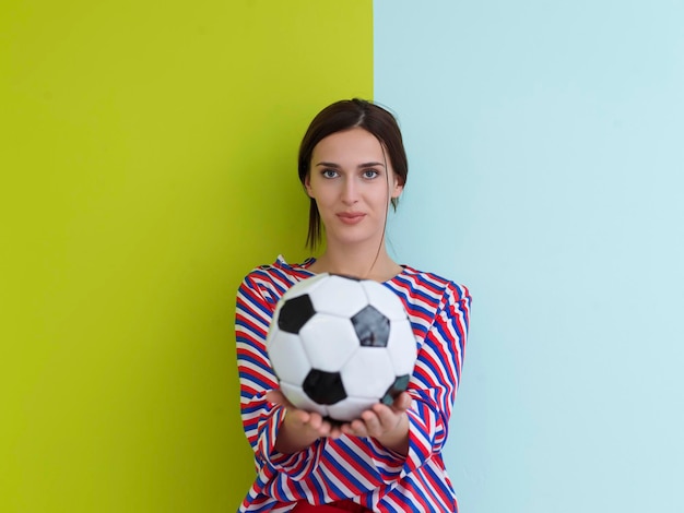 Portrait de jeune femme européenne tenant un ballon de football sur sa paume. Bonne fille, fan de football ou joueur isolé sur fond vert et bleu. Sport, jouer au football, santé, concept de mode de vie sain