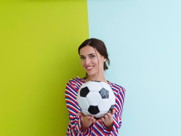 Portrait de jeune femme européenne tenant un ballon de football sur sa paume. Bonne fille, fan de football ou joueur isolé sur fond vert et bleu. Sport, jouer au football, santé, concept de mode de vie sain