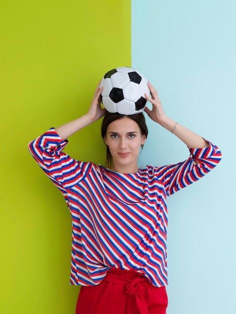 Portrait de jeune femme européenne tenant un ballon de football sur la tête. Bonne fille, fan de football ou joueur isolé sur fond vert et bleu. Sport, jouer au football, santé, concept de mode de vie sain