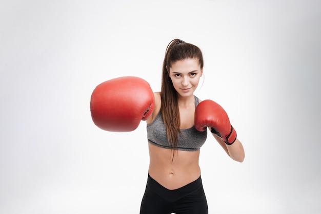 Portrait d'une jeune femme fitness frappant le devant avec des gants de boxe isolés