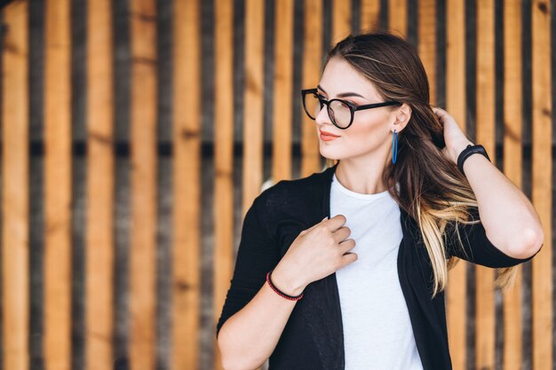 Portrait d'une jeune femme sur le fond en bois avec des planches verticales. Belle fille aux cheveux longs et lunettes souriant