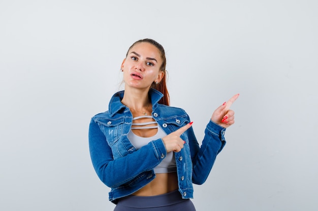 Portrait de jeune femme en forme pointant vers le coin supérieur droit en haut, veste en jean et à la vue de face triste