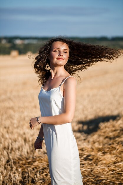 Portrait d'une jeune femme frisée dans un champ de blé, où le blé est fauché et les gerbes sont debout, profitant de la nature. La nature. rayons de soleil Agriculture