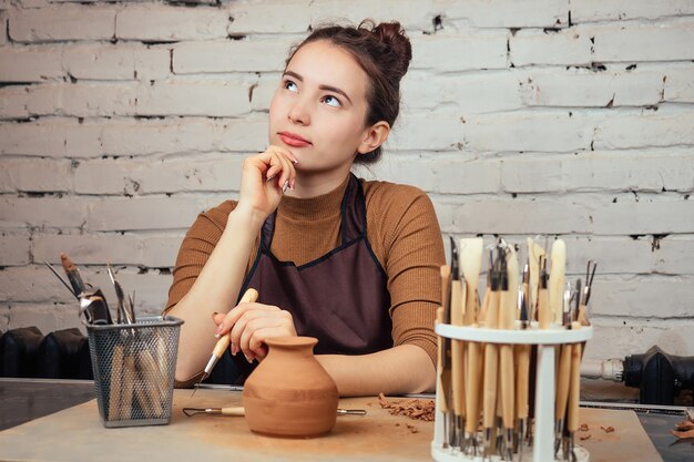 Portrait d'une jeune femme gaie tenant un vase d'argile. Le potier travaille dans un atelier de poterie avec de l'argile. le concept de l'artisanat et de la créativité d'un atelier de poterie.