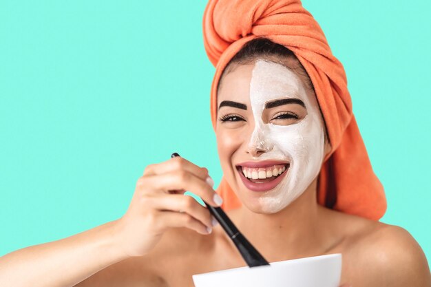 Portrait d'une jeune femme heureuse appliquant un masque facial sur un fond bleu