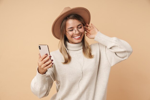 Portrait d'une jeune femme heureuse au chapeau dansant et écoutant de la musique avec un téléphone portable