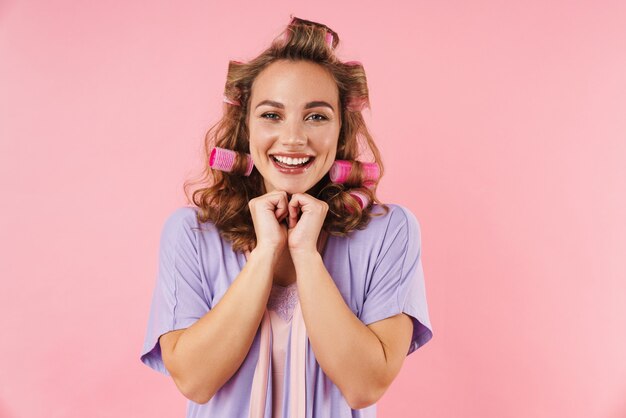 Portrait de jeune femme heureuse en bigoudis souriant isolé sur rose