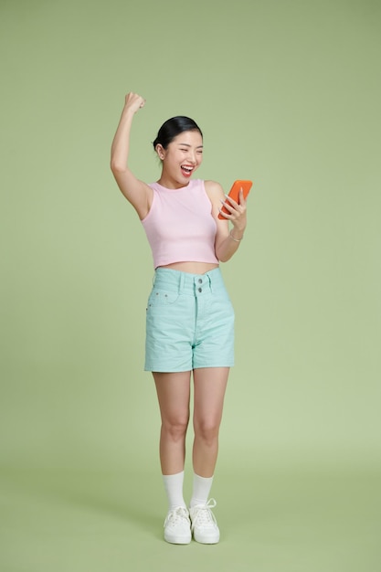 Portrait d'une jeune femme heureuse célébrant avec un téléphone portable isolé sur fond vert