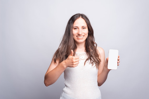 Portrait de jeune femme heureuse montrant le pouce vers le haut et écran mobile vide blanc