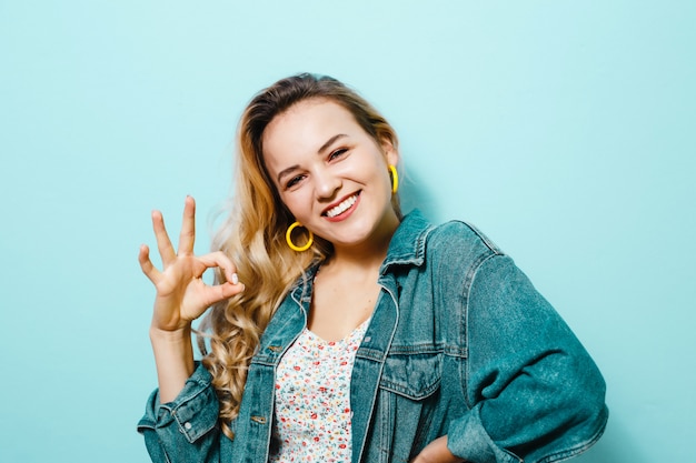 Portrait d'une jeune femme heureuse présentant des gestes et souriant sur mur bleu