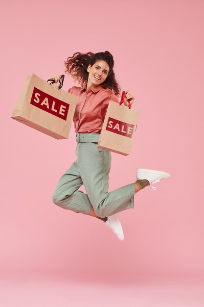 Portrait de jeune femme heureuse de son shopping réussi, elle saute sur le fond rose