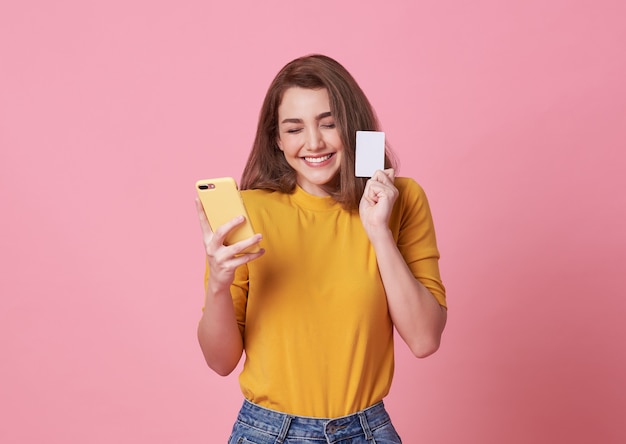 Portrait d'une jeune femme heureuse tenant un téléphone portable et une carte de crédit isolée sur rose.