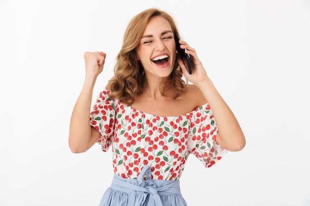 Portrait d'une jeune femme heureuse vêtue de vêtements d'été se réjouissant et riant tout en parlant au téléphone portable isolé