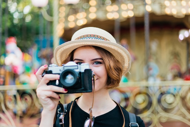 Portrait d'une jeune femme hipster dans un chapeau avec un appareil photo rétro dans un parc d'attractions