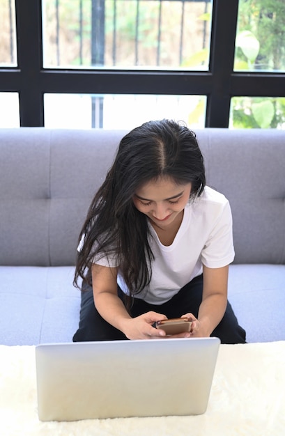 Portrait d'une jeune femme indépendante travaillant avec un ordinateur portable et utilisant un téléphone portable dans le salon.