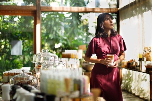 Photo portrait de jeune femme indienne dans un café avec un environnement relaxant, peau bronzée femme asiatique robe violette se sentir sourire heureux dans la nature calme et café glacé avec le soleil du matin à travers le rideau de dentelle