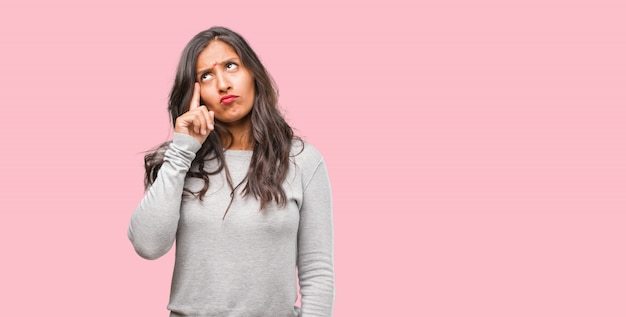 Portrait de jeune femme indienne pensant et levant les yeux, confuse à propos d&#39;une idée