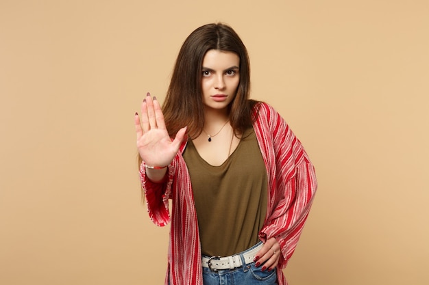 Portrait d'une jeune femme inquiète en vêtements décontractés montrant un geste d'arrêt avec paume isolée sur fond de mur beige pastel en studio. Les gens émotions sincères, concept de style de vie. Maquette de l'espace de copie.