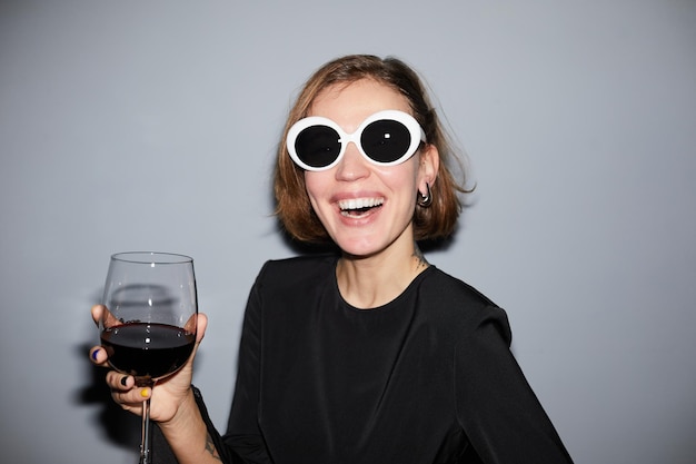 Portrait d'une jeune femme insouciante faisant la fête et tenant un verre de vin tout en portant des lunettes de soleil prises avec un flash