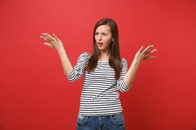 Portrait d'une jeune femme irritée et inquiète dans des vêtements décontractés à rayures debout, écartant les mains