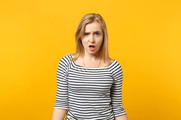 Portrait d'une jeune femme irritée et perplexe dans des vêtements rayés regardant la caméra, jurant isolé sur fond orange jaune en studio. Émotions sincères des gens, concept de style de vie. Maquette de l'espace de copie.