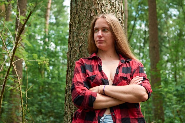 Un portrait de jeune femme italienne avec les bras croisés portant une flanelle rouge dans une forêt