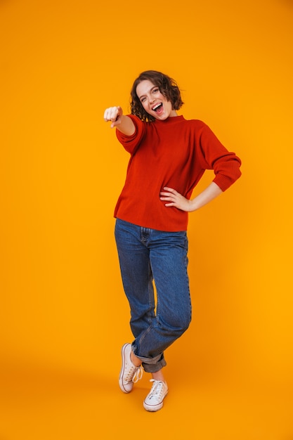 portrait d'une jeune femme jolie heureuse posant isolé sur un mur jaune pointant vers vous.