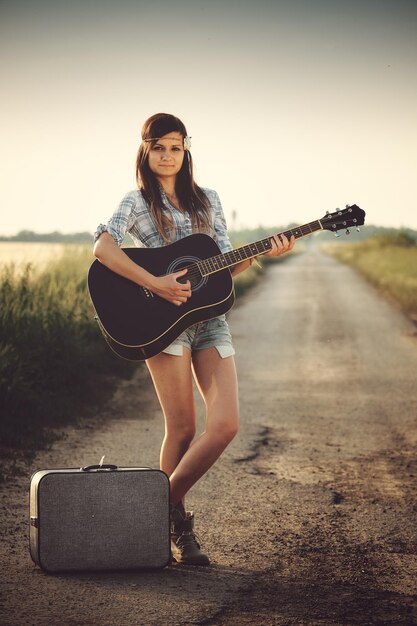 Portrait d'une jeune femme jouant de la guitare alors qu'elle se tient sur la route