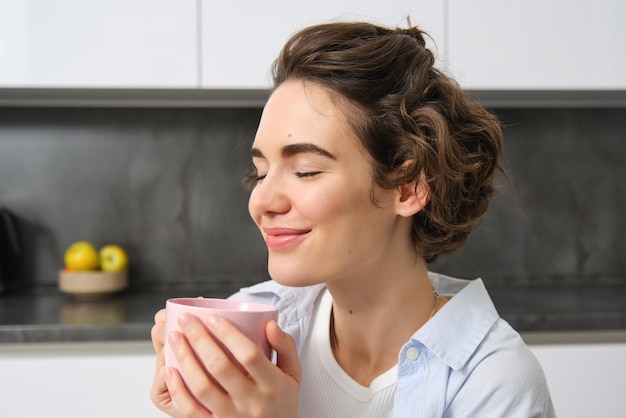 Portrait d'une jeune femme joyeuse dégustant une tasse de café à la maison souriante belle fille boit chaud