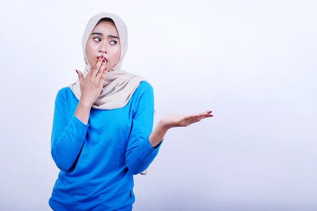 Portrait de jeune femme joyeuse avec t-shirt bleu portant le hijab montrant quelque chose, surprenant et ferme la bouche