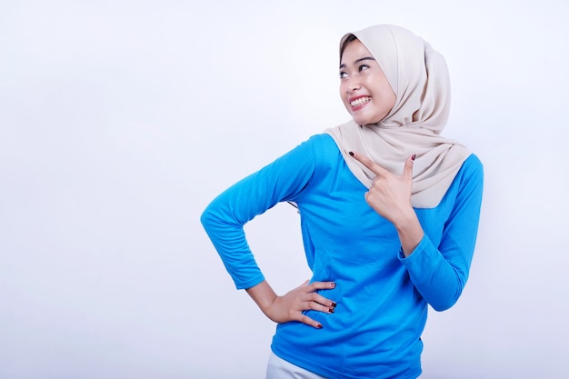 Portrait de jeune femme joyeuse avec t-shirt bleu portant le hijab, se sentir heureux et pointant vers la gauche