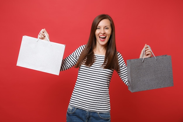 Portrait d'une jeune femme joyeuse en vêtements rayés tenant des sacs de paquets avec des achats après le shopping isolé sur fond de mur rouge. Les gens émotions sincères, concept de style de vie. Maquette de l'espace de copie.