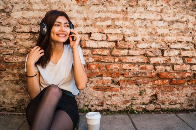 Portrait de jeune femme latine se détendre et écouter de la musique avec des écouteurs sur le mur de briques. Concept urbain.