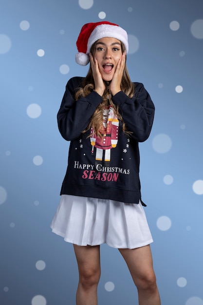 Portrait d'une jeune femme latine surprise avec un pull de noël et un chapeau de père noël