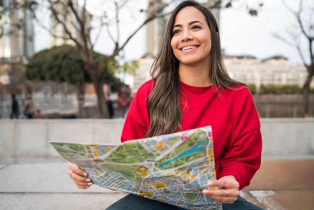 Portrait de jeune femme latine tenant une carte et à la recherche de directions à l'extérieur dans la rue. Concept de voyage.