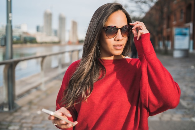 Portrait de jeune femme latine tenant son téléphone portable à l'extérieur dans la rue. Concept urbain.