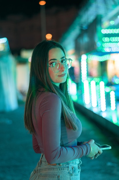 Portrait d'une jeune femme à lunettes illuminée par les lumières d'une fête foraine