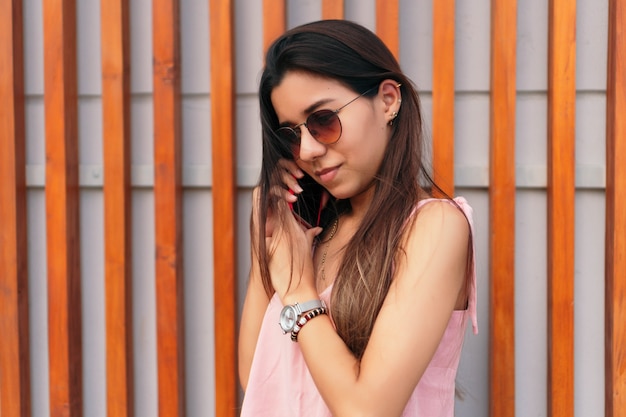 Portrait d'une jeune femme avec des lunettes de soleil parlant sur son téléphone portable à l'extérieur