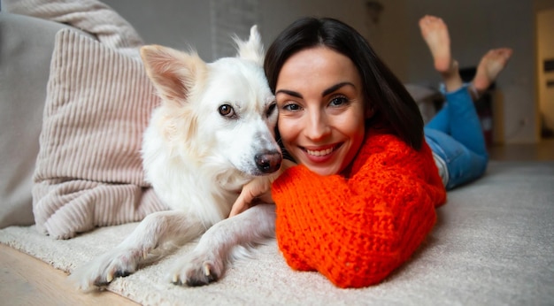 Portrait d'une jeune femme magnifique et heureuse étreignant son gros chien blanc mignon allongé sur un tapis à l'étage de la maison