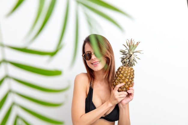 Portrait de jeune femme en maillot de bain et lunettes à l'ananas sur fond blanc. Concept d'image de saison d'été