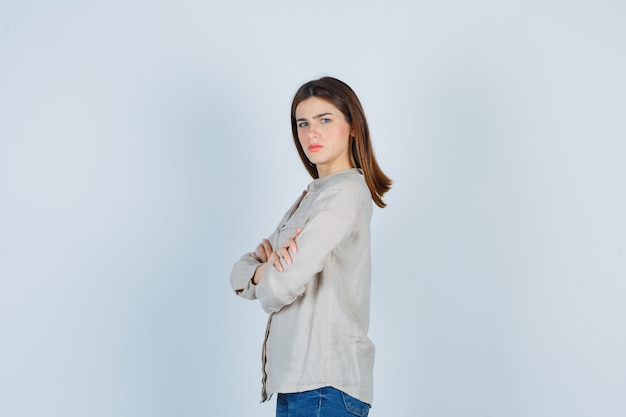 Portrait de jeune femme avec les mains croisées en jeans décontractés et l'air mécontent