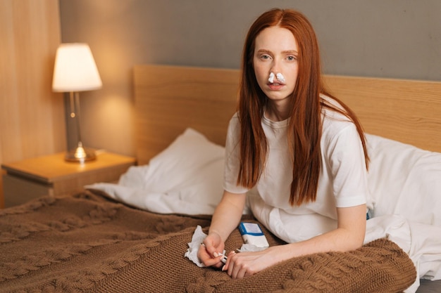 Portrait d'une jeune femme malade souffrant de la maladie du nez qui coule mouchoirs en papier insérés dans le nez en regardant la caméra