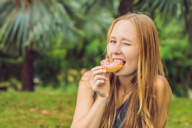 Portrait d'une jeune femme mangeant un beignet sur un fond végétal.