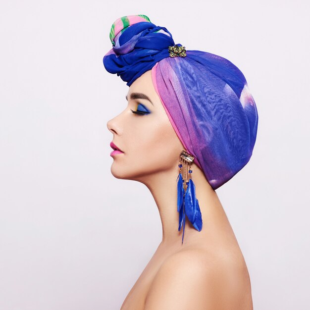 Portrait d'une jeune femme avec un maquillage lumineux et un foulard à la mode sur un mur clair.