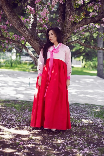 Portrait jeune femme une mariée coréenne en costumes nationaux debout près de l'arbre de fleurs de cerisier au printemps