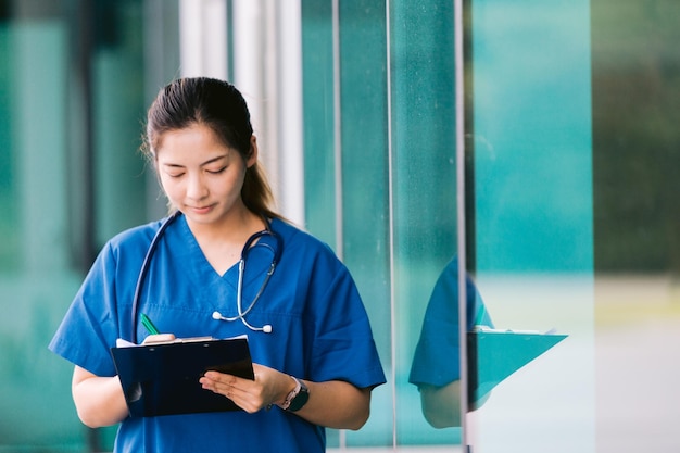 Portrait de jeune femme médecin asiatique écrit sur presse-papiers dans le couloir de l'hôpital