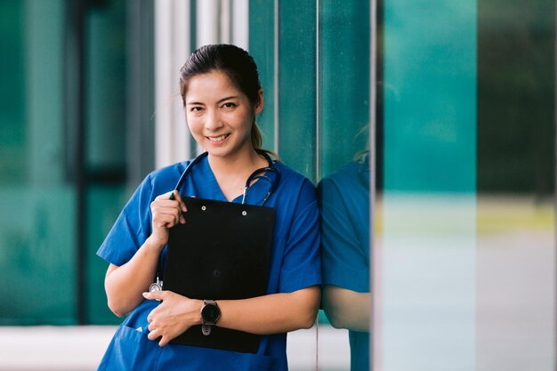 Portrait de jeune femme médecin asiatique écrit sur presse-papiers dans le couloir de l'hôpital