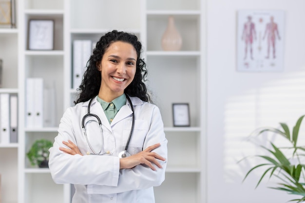 Portrait d'une jeune femme médecin belle et prospère à l'intérieur du cabinet médical femme hispanique avec des boucles